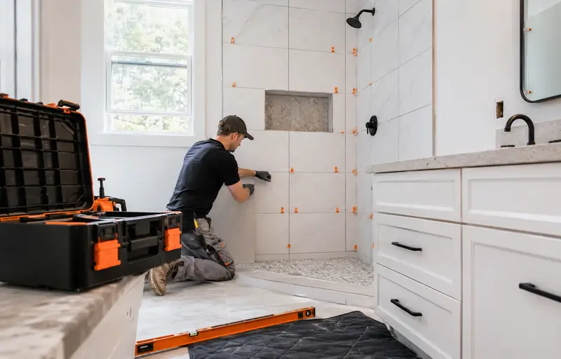 Contractor setting tile in a newly renovated bathroom with a glass walk-in shower